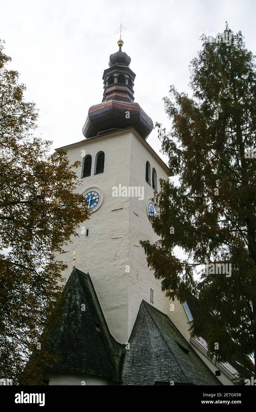 Storico campanile della chiesa con cupola a cipolla barocca e volti dell'orologio tra alberi autunnali Foto Stock