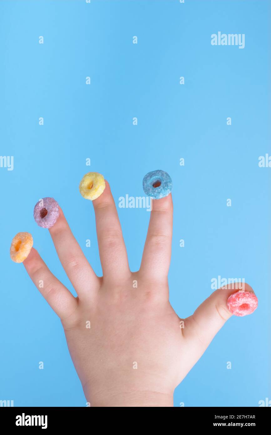 Cereali colorati rotondi nelle dita di un bambino su sfondo blu. La colazione è variopinta Foto Stock
