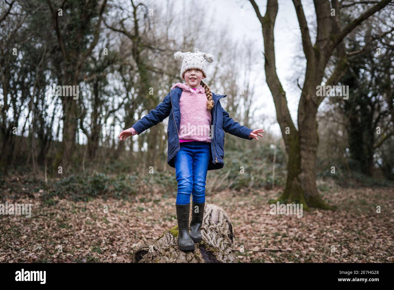 Eccitata giovane ragazza felice in stivali wellinton sedette in autunno campagna equilibrando su tronco di albero con le armi fuori esplorare il grande parco naturale all'aperto Foto Stock