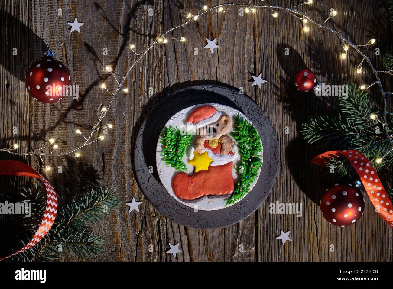 Pan di zenzero decorato con carattere di orso e stivale Santa. Piatto natalizio con ramoscelli in abete, baubles rossi e luci natalizie. Tavole di legno scuro Foto Stock