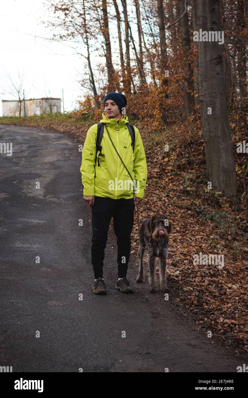 Giovane uomo in giacca gialla di 20-24 anni in una passeggiata con baffi cechi, un cane da caccia. Ritratto binario di prendersi cura dell'animale domestico, dell'amore e della relazione. Foto Stock