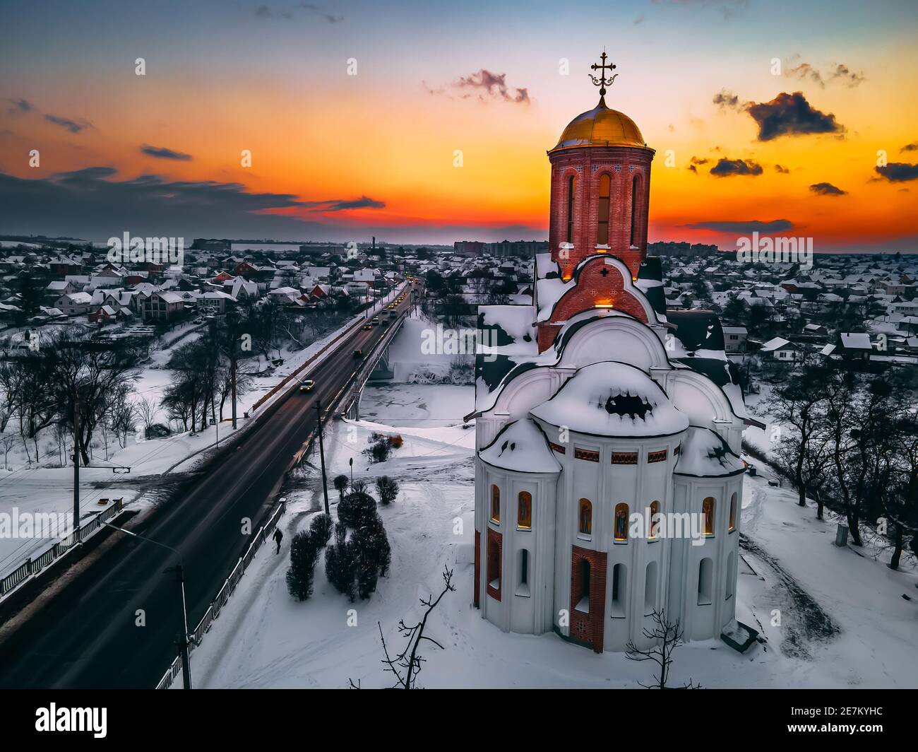 Vista aerea della chiesa in una piccola città europea coperta di neve al luminoso tramonto d'inverno, splendidi tramonti e nuvole. Drone. Inverno. Ucraina, 2021 Foto Stock