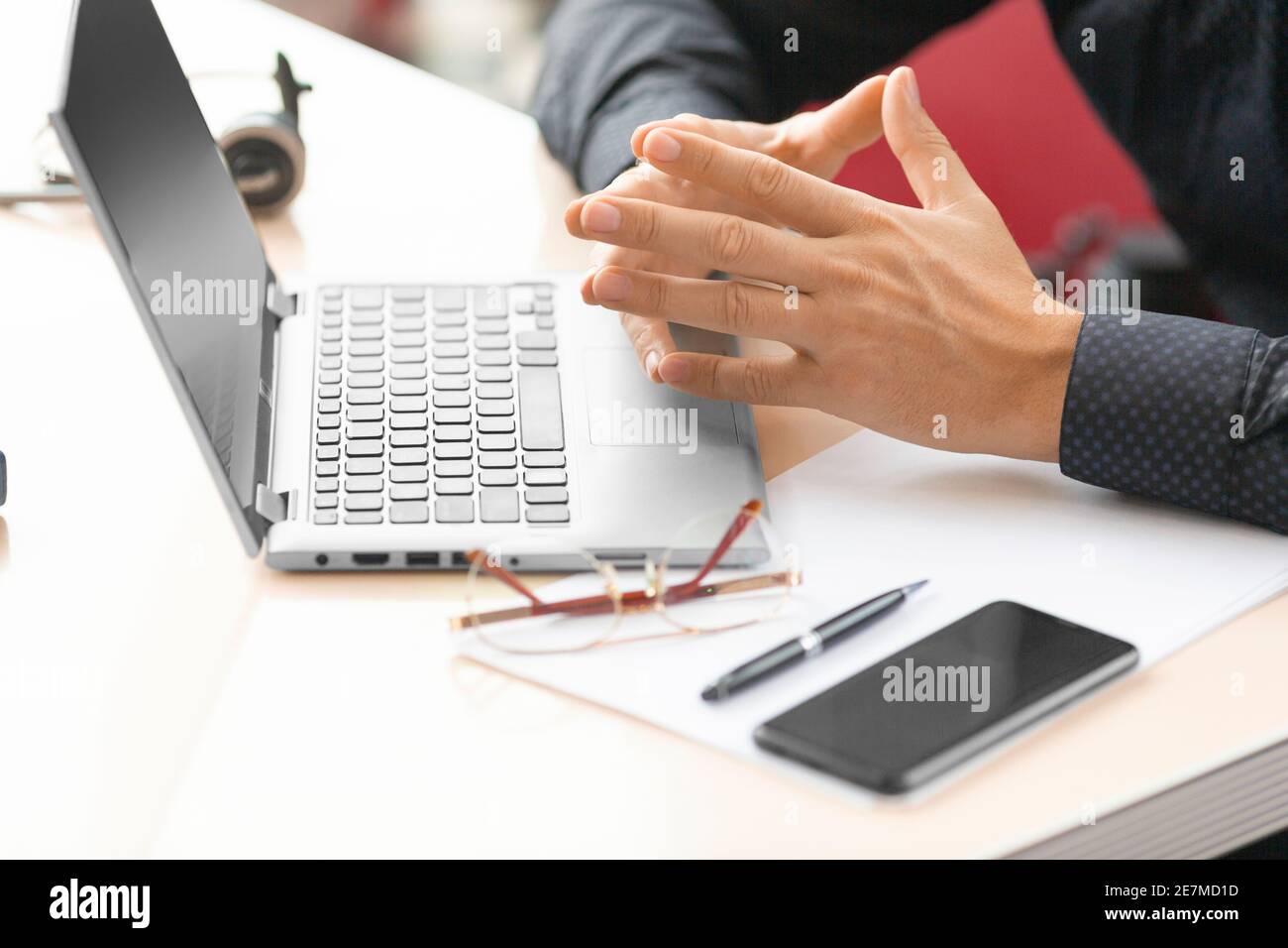 Un uomo d'affari davanti a un monitor portatile durante una consultazione online con un ispettore fiscale. Primo piano su mani, telefono e accessori. Foto Stock
