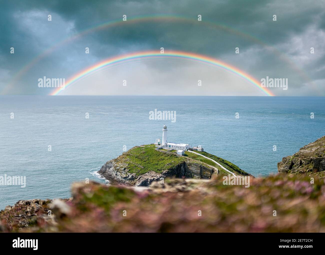 Colorati doppi arcobaleni in mare sopra l'orizzonte dell'oceano con tempesta nuvole cielo drammatico e bianco faro in cima a sud stack isola costa Foto Stock