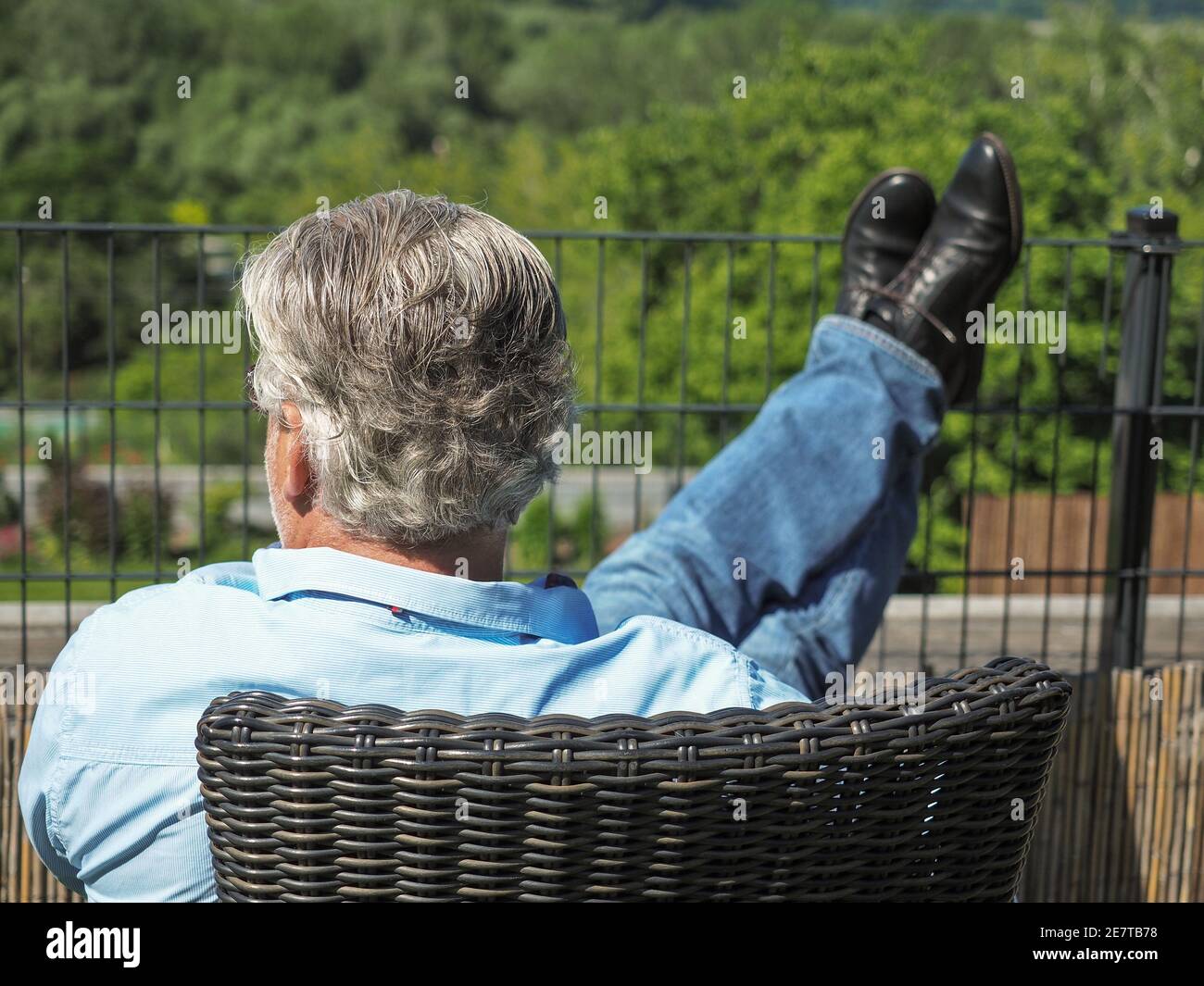 Uomo d'affari caucasico senior con capelli grigi seduti in giardino. Giorno di primavera soleggiato. Foto Stock