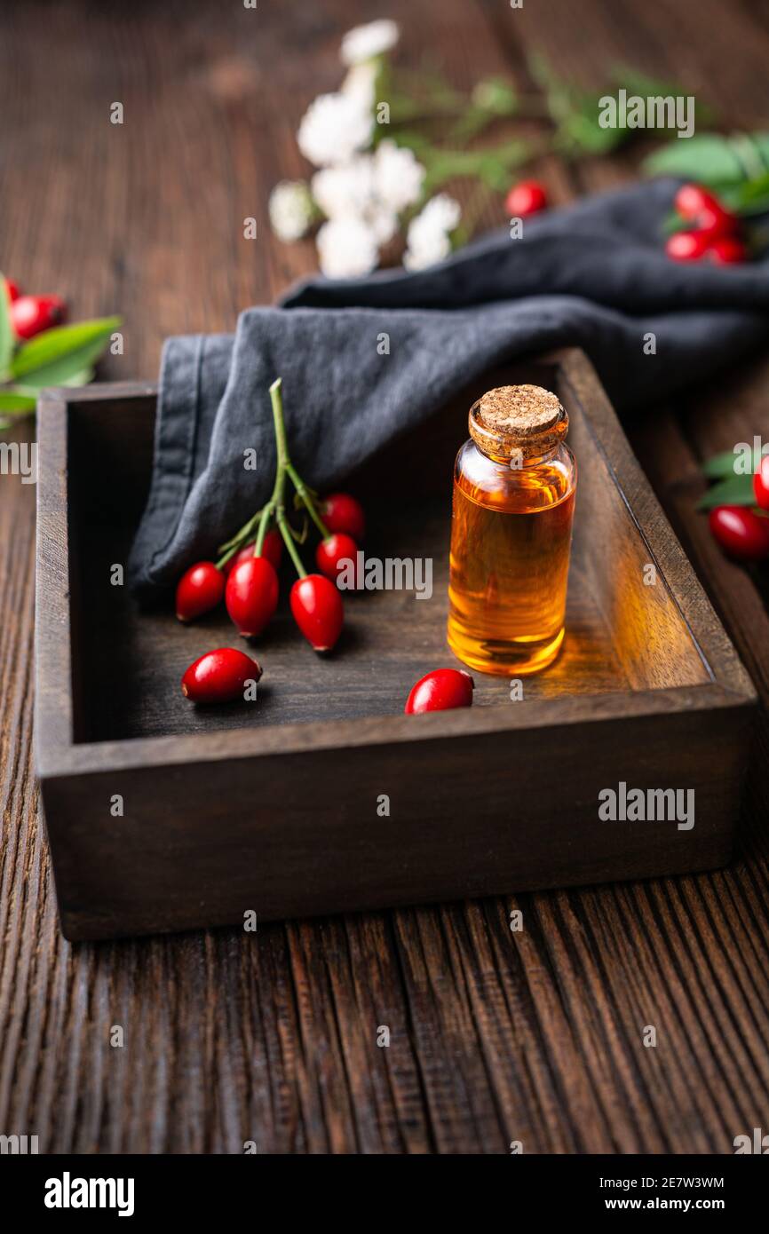 Olio di semi di rosa canina puro in una bottiglia di vetro, rimedio per la pelle e i capelli su fondo rustico di legno Foto Stock