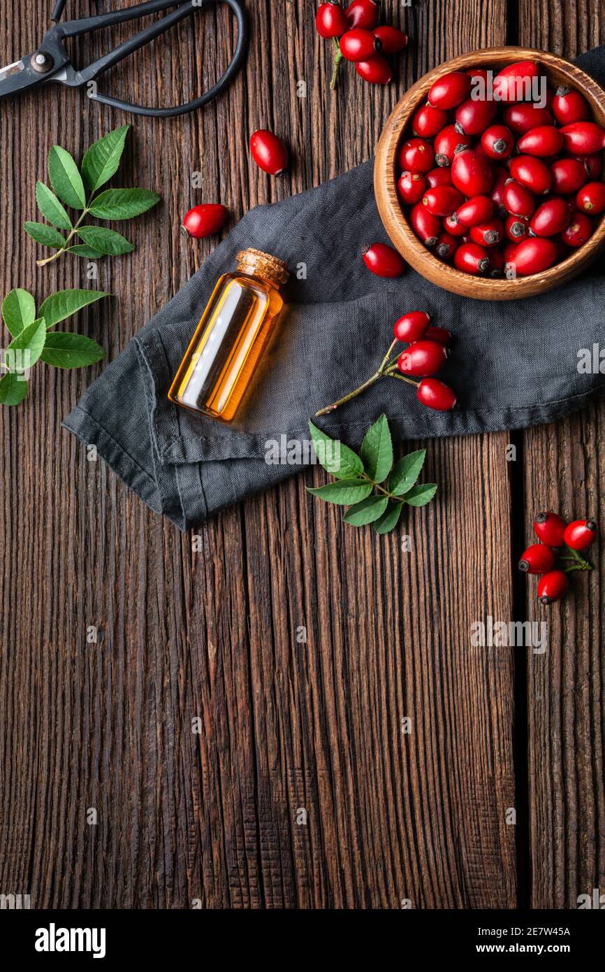 Olio di semi di rosa canina puro in una bottiglia di vetro, rimedio per la pelle e i capelli su fondo rustico di legno con spazio di copia Foto Stock
