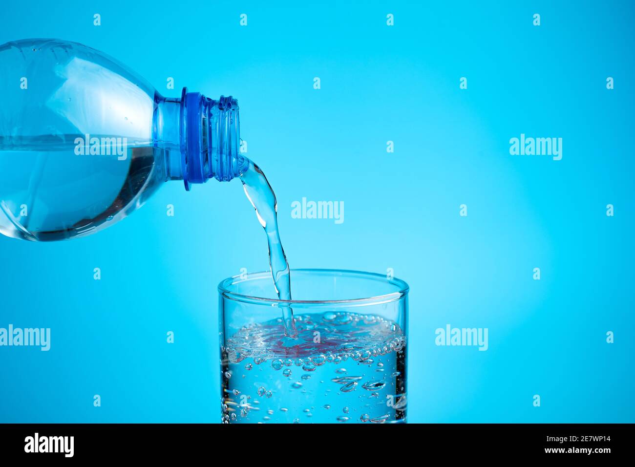 Il processo di versamento dell'acqua in un bicchiere su un sfondo blu Foto Stock