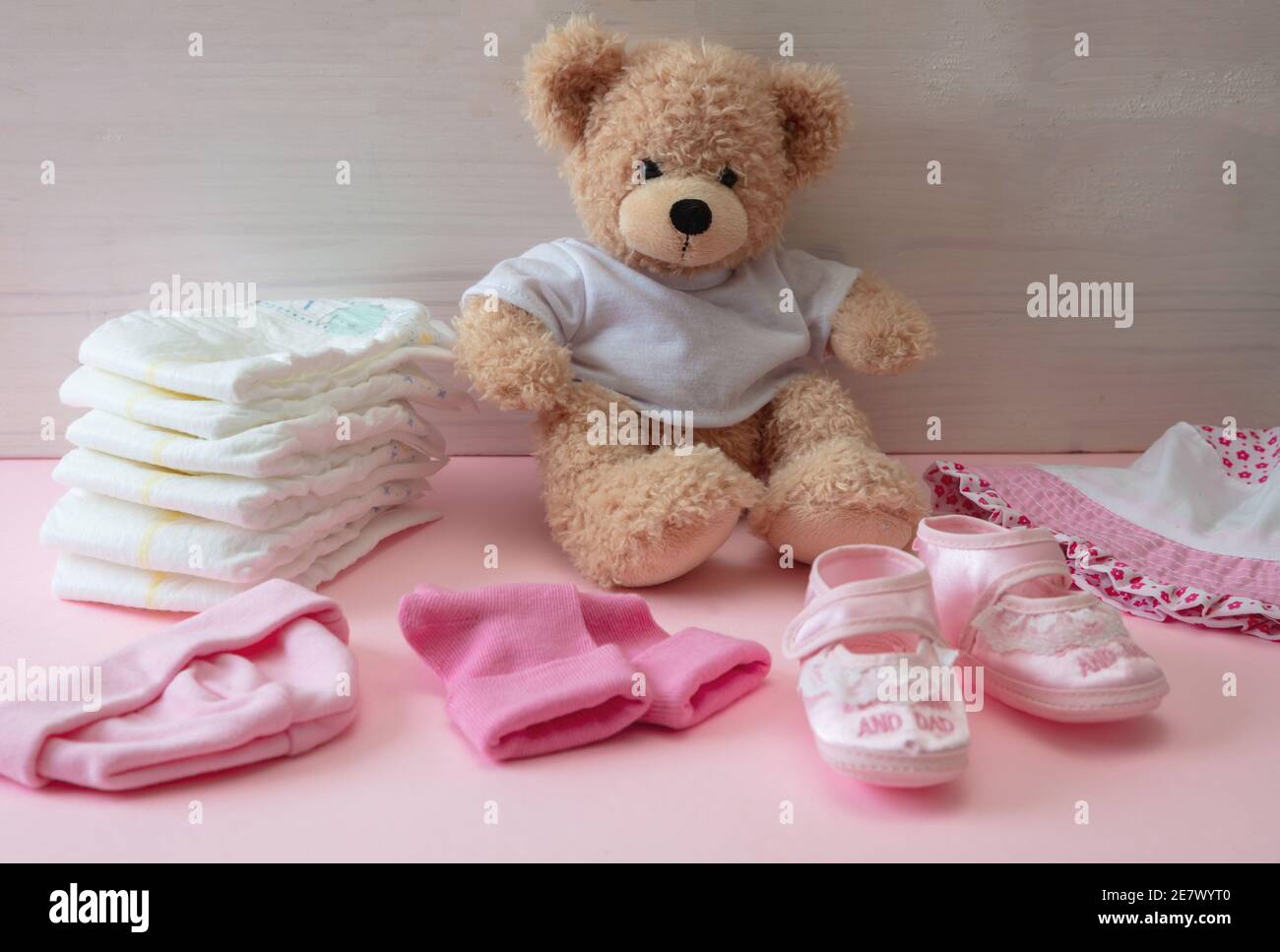 Accessori per bambina. Carino orsacchiotto seduto su pavimento di colore rosa, sfondo di legno muro. Forniture per bambine, pannolini, scarpe, abbigliamento Foto Stock