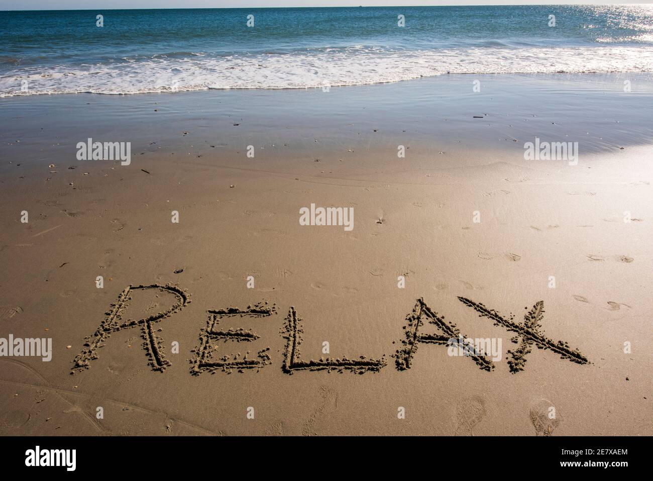 La parola RELAX scritta nella sabbia vicino al mare. Foto Stock