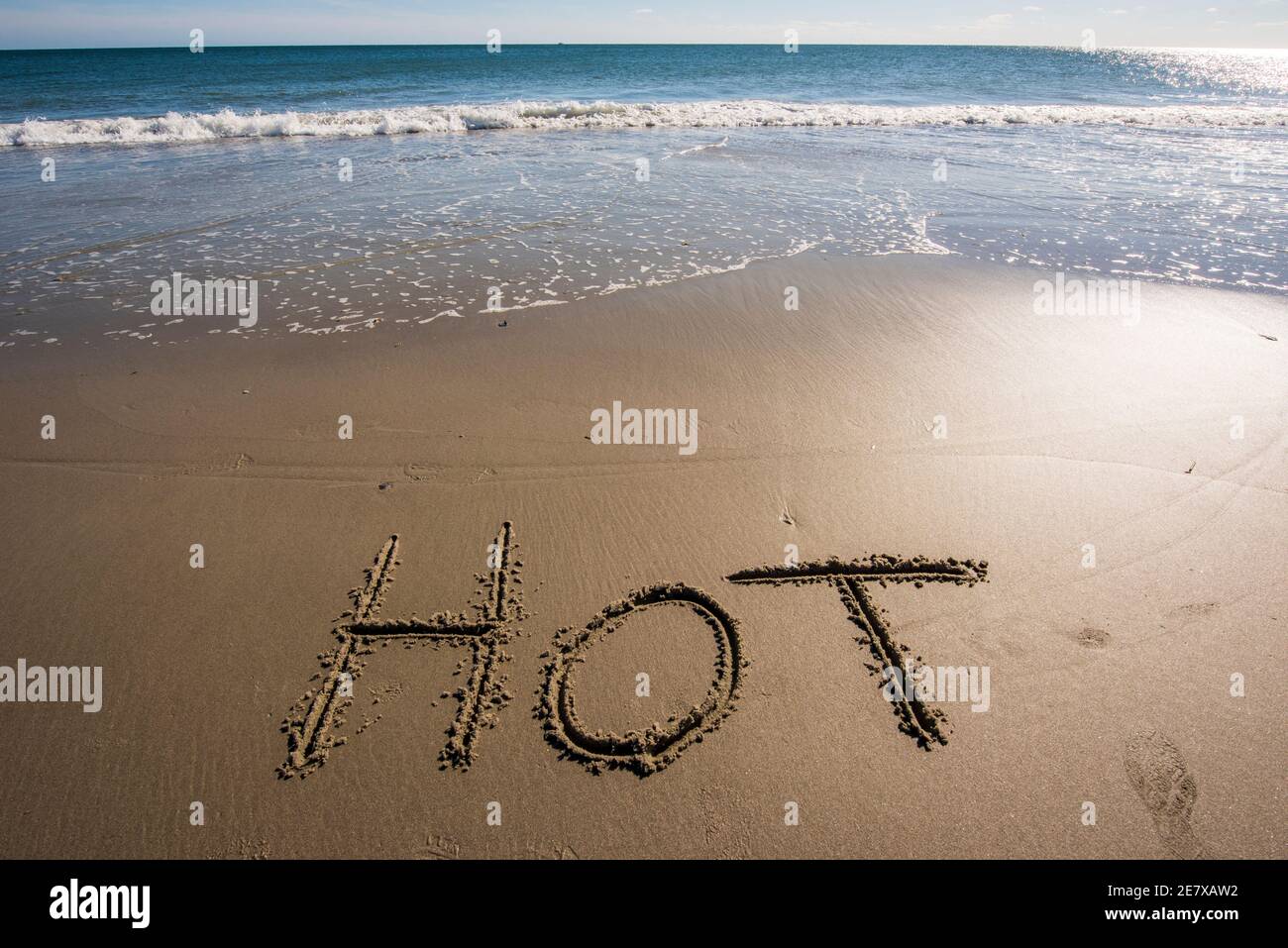 La parola CALDO scritta nella sabbia vicino al mare. Foto Stock