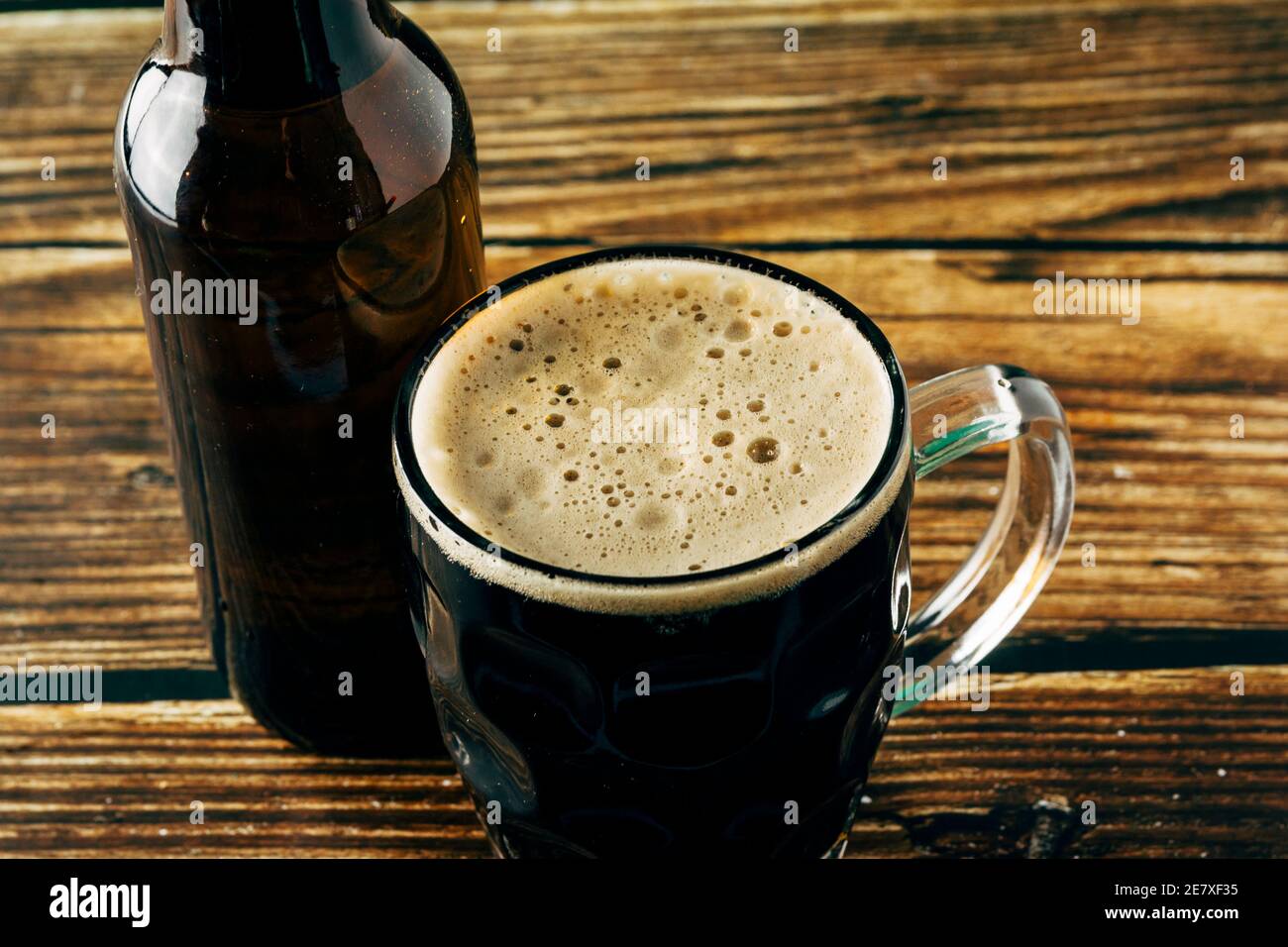 Primo piano della schiuma di una birra scura servita in una tazza su un tavolo di legno. St. Patrick e Stout Concept Foto Stock