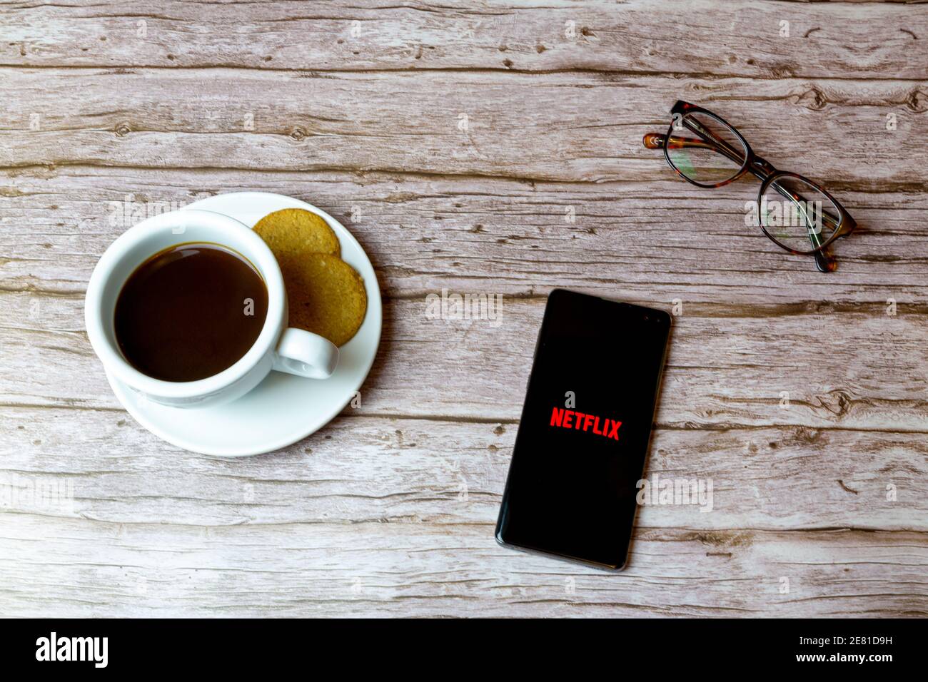 Un telefono cellulare o un telefono cellulare posato su un legno Tavolo con l'app Netflix che apre anche un caffè e. occhiali Foto Stock