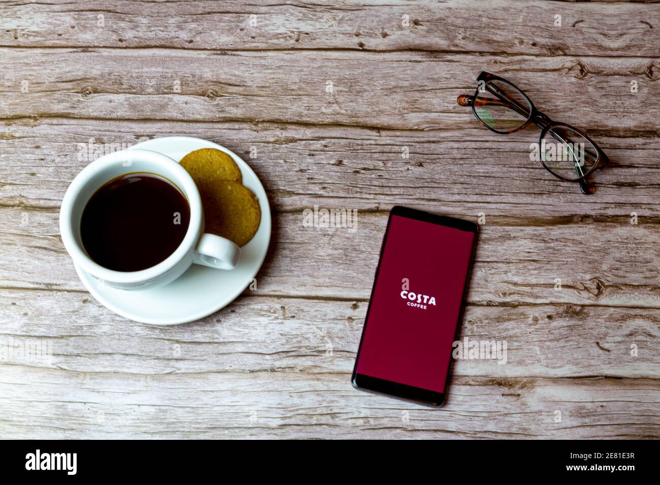 Un telefono cellulare o un telefono cellulare posato su un legno Tavolo con l'app Costa Coffee che apre anche un caffè e bicchieri Foto Stock