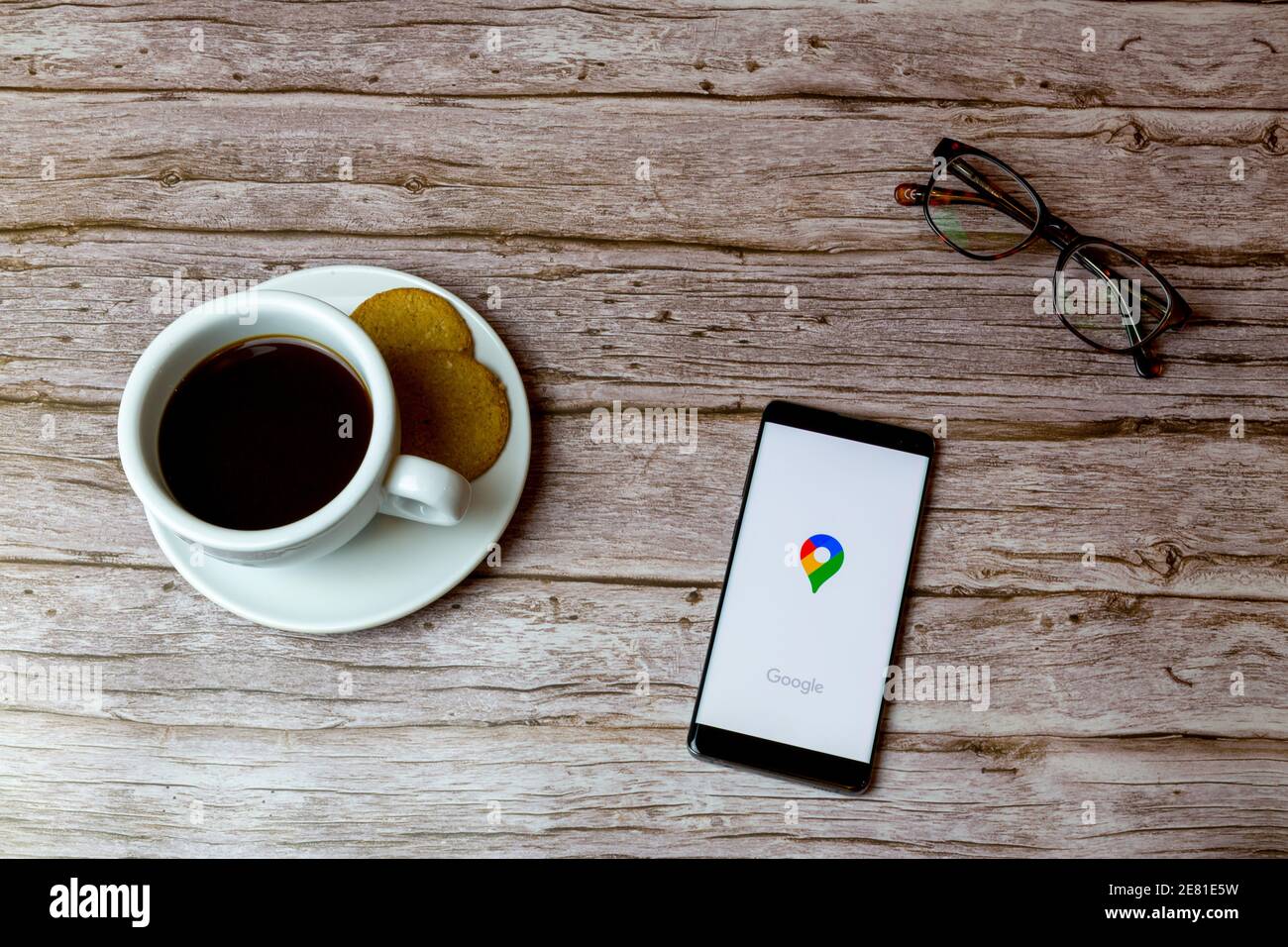 Un telefono cellulare o un telefono cellulare posato su un legno Tabella con l'app Google Maps che apre anche un caffè e. occhiali Foto Stock