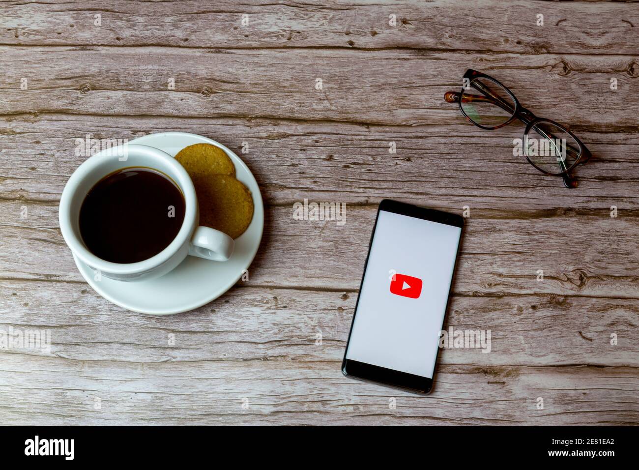 Un telefono cellulare o un telefono cellulare posato su un legno Tavolo con l'app YouTube che apre anche un caffè e. occhiali Foto Stock