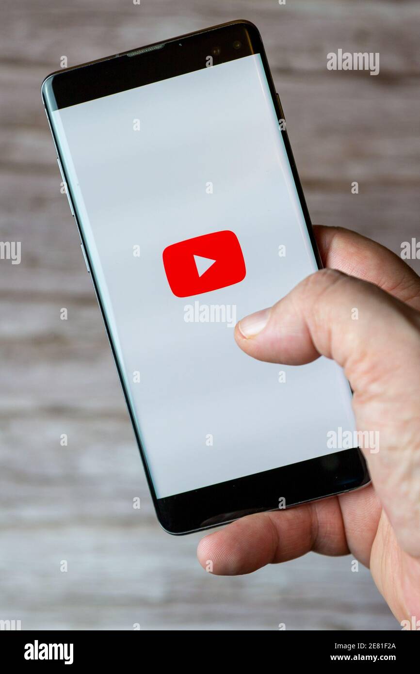 Una mano che tiene un telefono cellulare o cellulare con L'app YouTube si apre sullo schermo Foto Stock