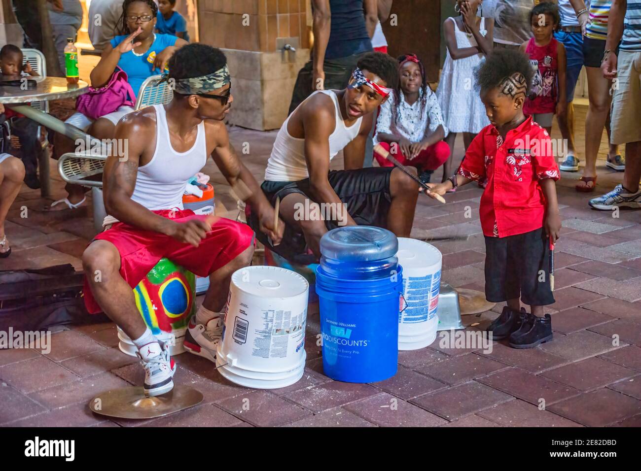 I musicisti di strada suonano la batteria improvvisata con l'aiuto di un ragazzino al Bayfront Marketplace situato sulla Biscayne Bay a Miami, Florida. Foto Stock