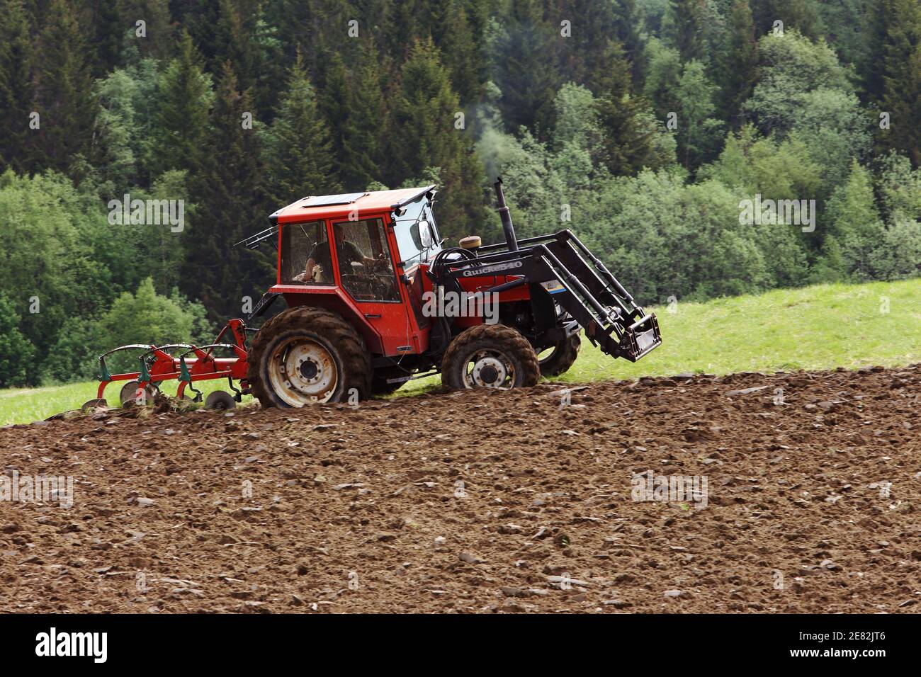 Klaebu, Norvegia - 23 maggio 2014: Un piccolo trattore rosso coperto Quicke 540 aratura il campo. Foto Stock