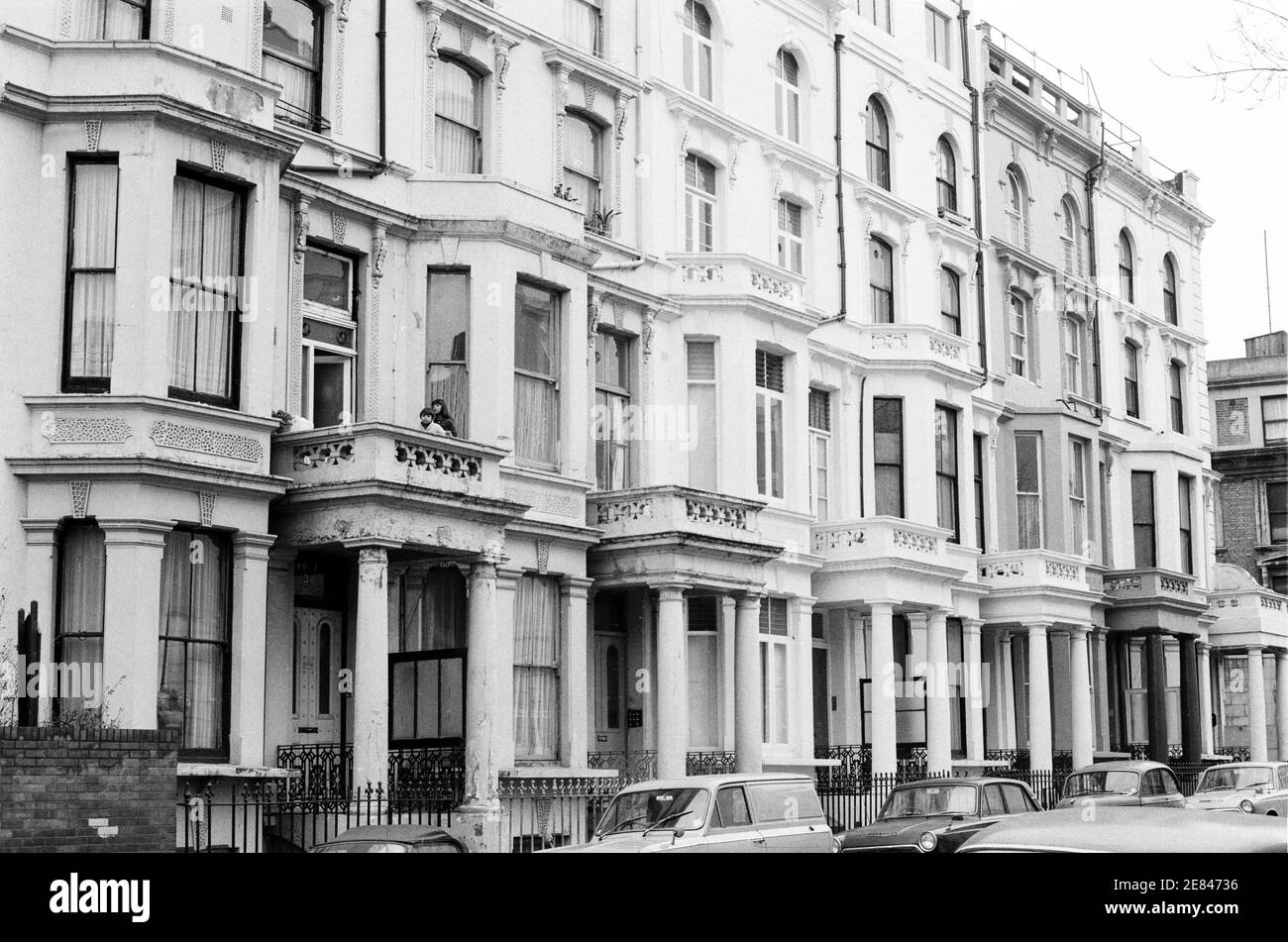 UK, West London, Notting Hill, 1973. Rundown e faticosamente grandi case a quattro piani stanno iniziando ad essere restaurate e ridecorate. Alloggio che include No.36 Powis Square, Talbot Road sulla destra. I bambini si affacciano da un balcone su una casa che ha bisogno di manutenzione. Foto Stock