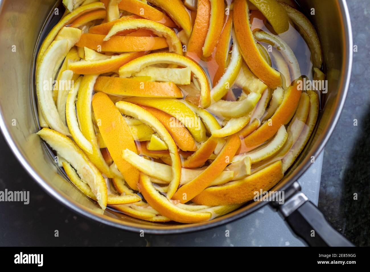 Bucce di arancia e limone fette e poste in una padella di wether bollente e zucchero per fare bucce candite Foto Stock