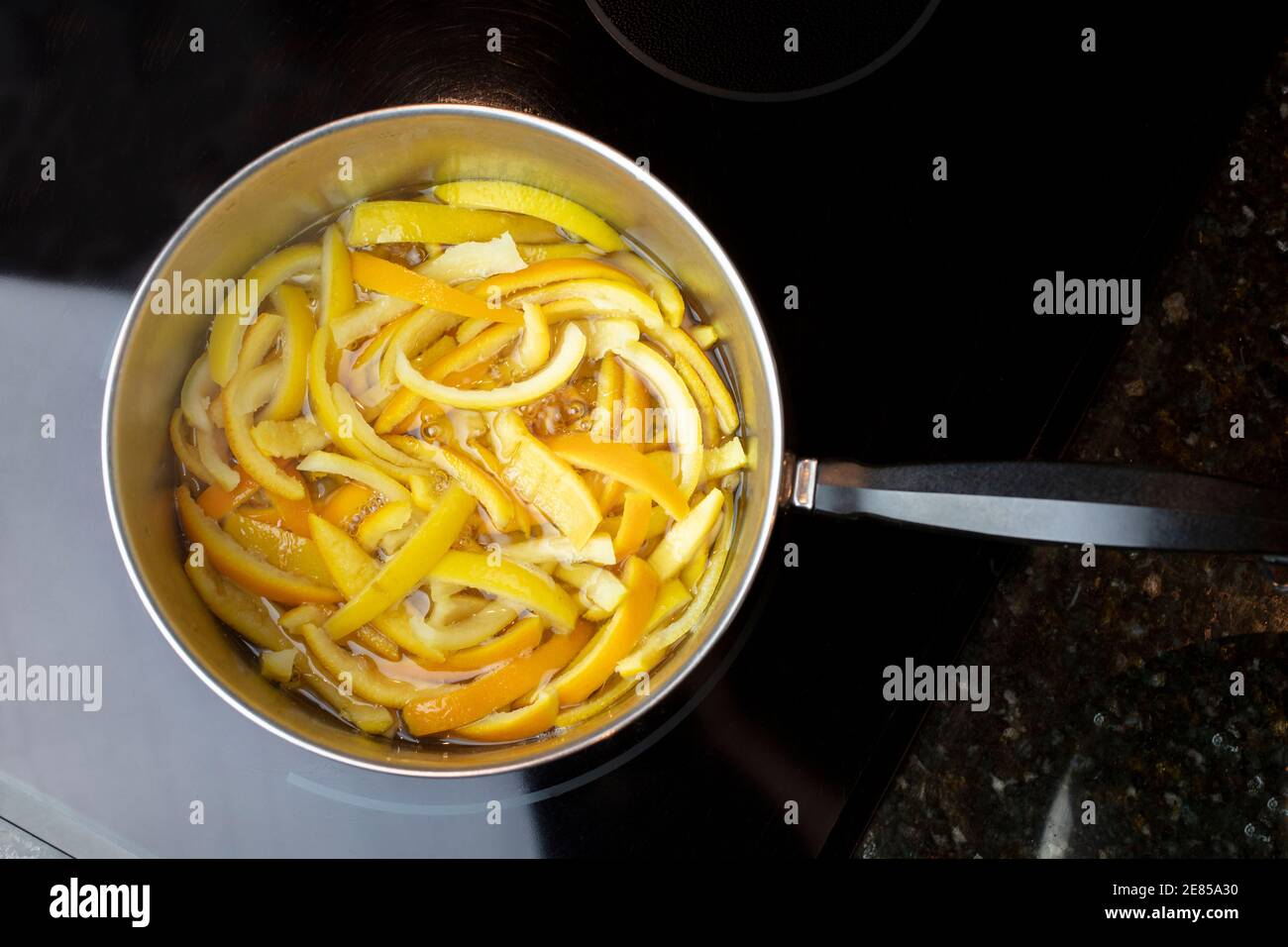 Bucce di arancia e limone fette e poste in una padella di wether bollente e zucchero per fare bucce candite Foto Stock