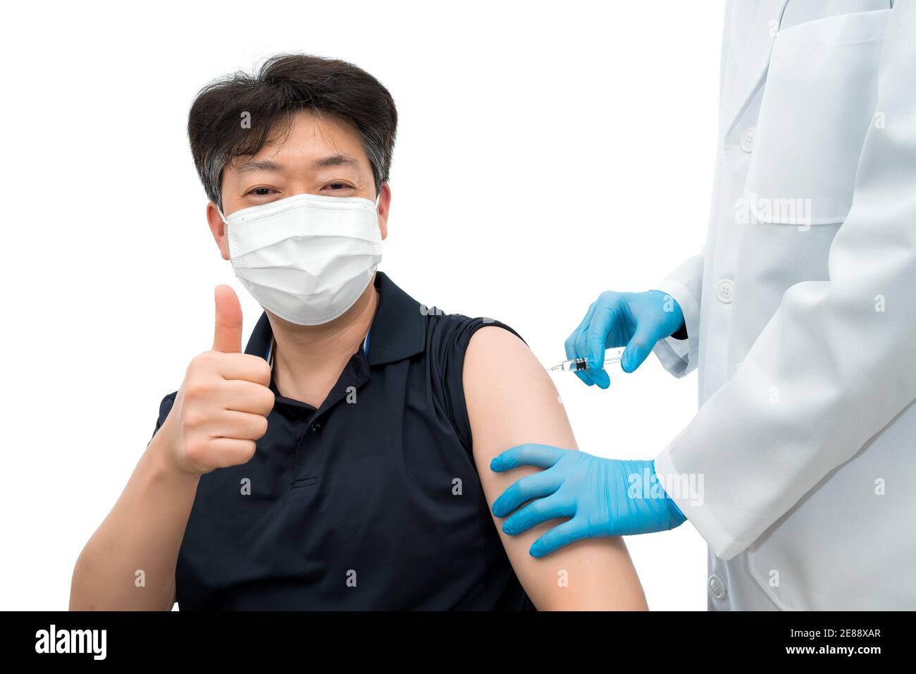 Un medico che tiene sotto controllo una siringa dà un'iniezione di vaccino ad un paziente asiatico di mezza età che indossa una maschera medica. Foto Stock