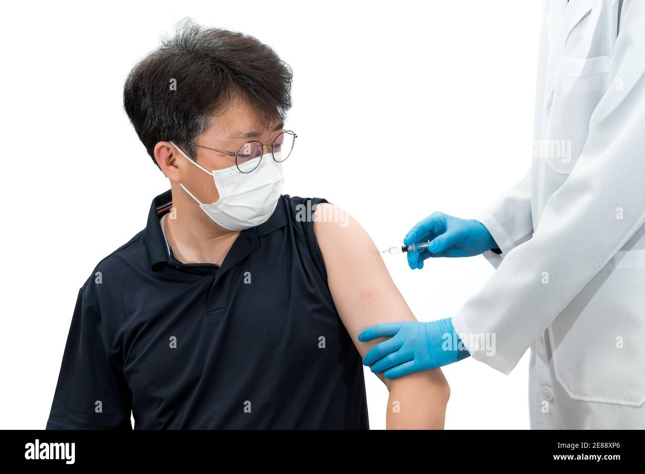 Un medico che tiene sotto controllo una siringa dà un'iniezione di vaccino ad un paziente asiatico di mezza età che indossa una maschera medica. Foto Stock
