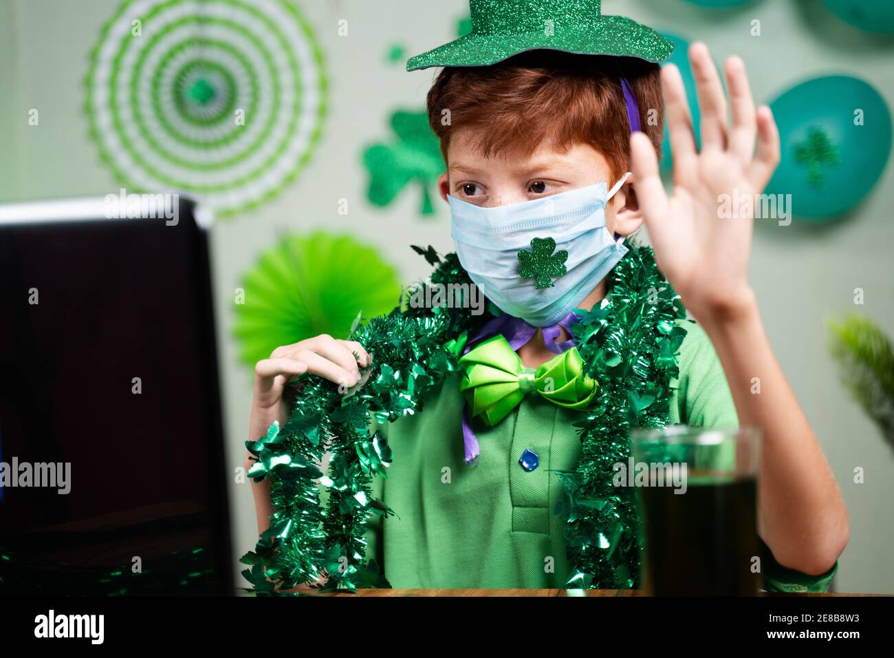 Bambino giovane con maschera facciale occupato in videochiamata su Laptop - concetto di San Patrizio lontano giorno celebrazione due a coronavirus o covid-19 pandemia Foto Stock