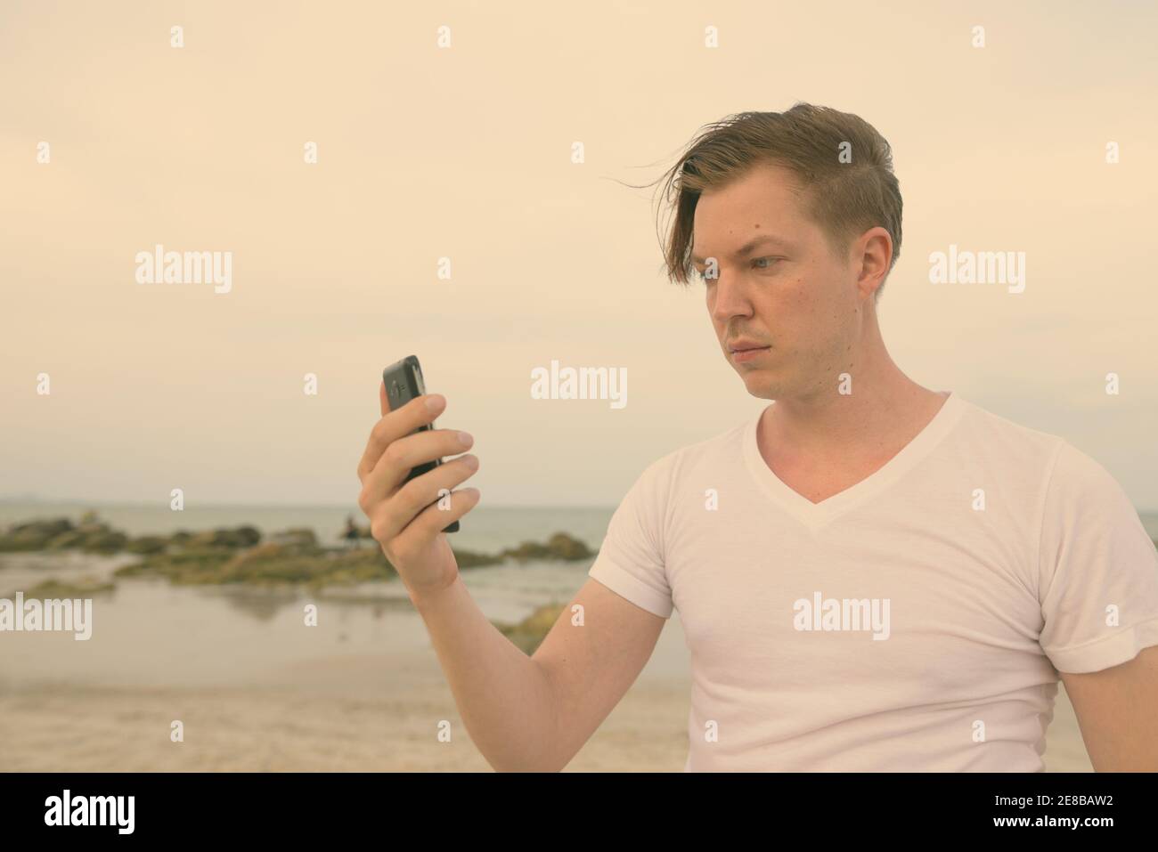 Giovane uomo bello utilizzando il telefono cellulare presso la spiaggia pubblica di Hua Hin in Thailandia Foto Stock