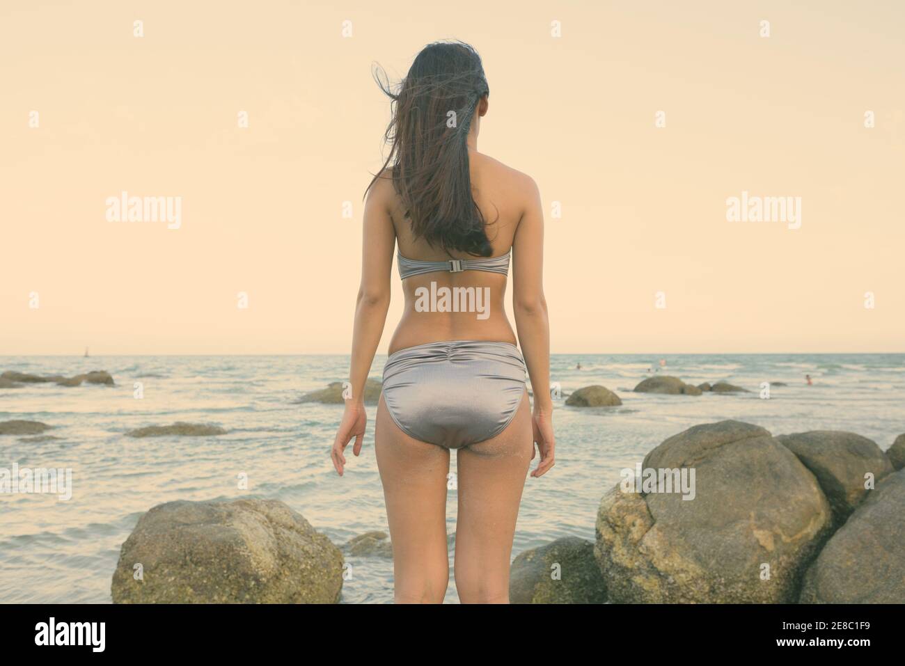 Vista posteriore del giovane bella donna asiatica in piedi sulle rocce della spiaggia pubblica in Hua Hin Tailandia Foto Stock