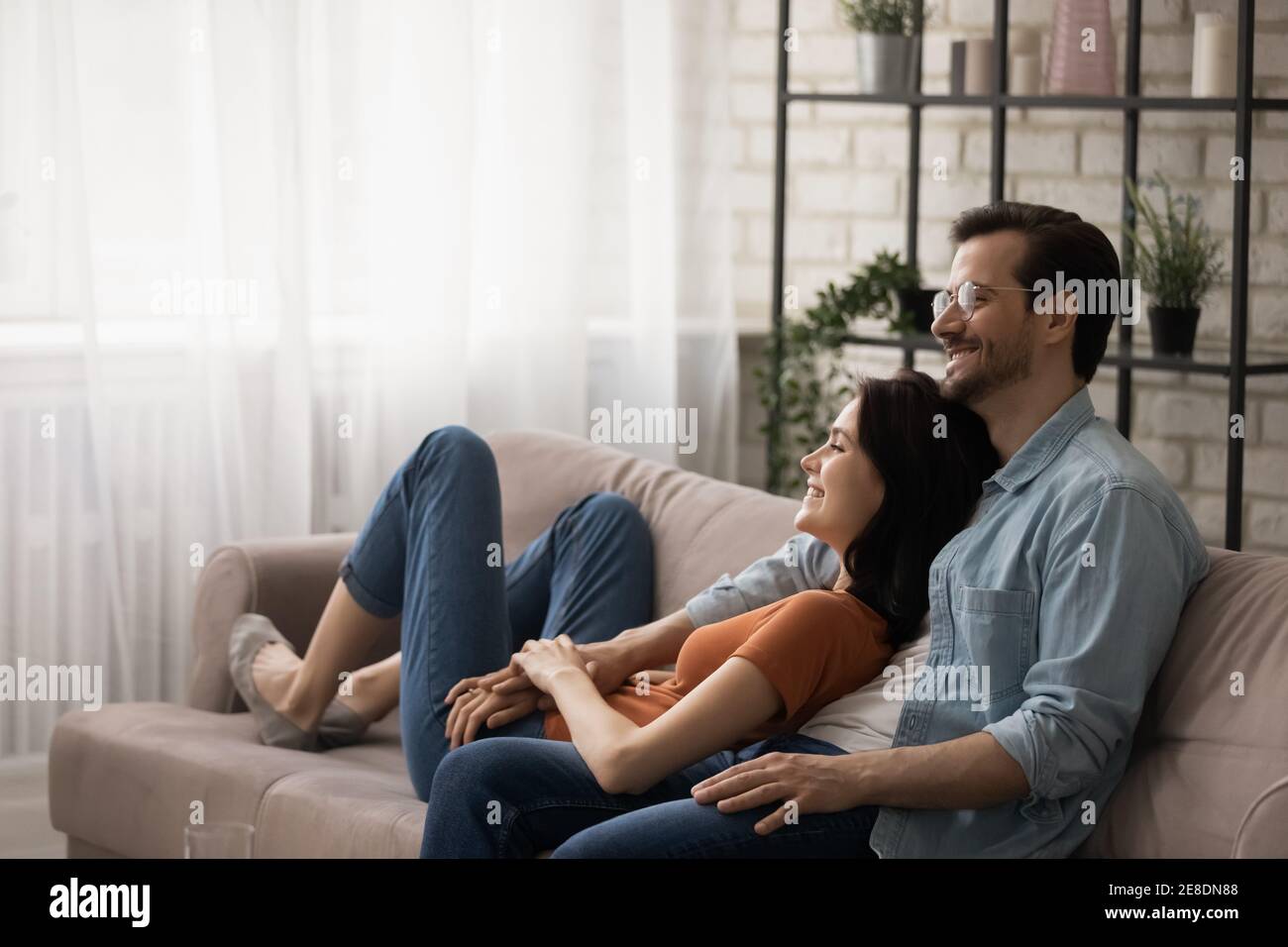 Felice giovane coppia sognante abbracciando, rilassandosi su un divano accogliente insieme Foto Stock