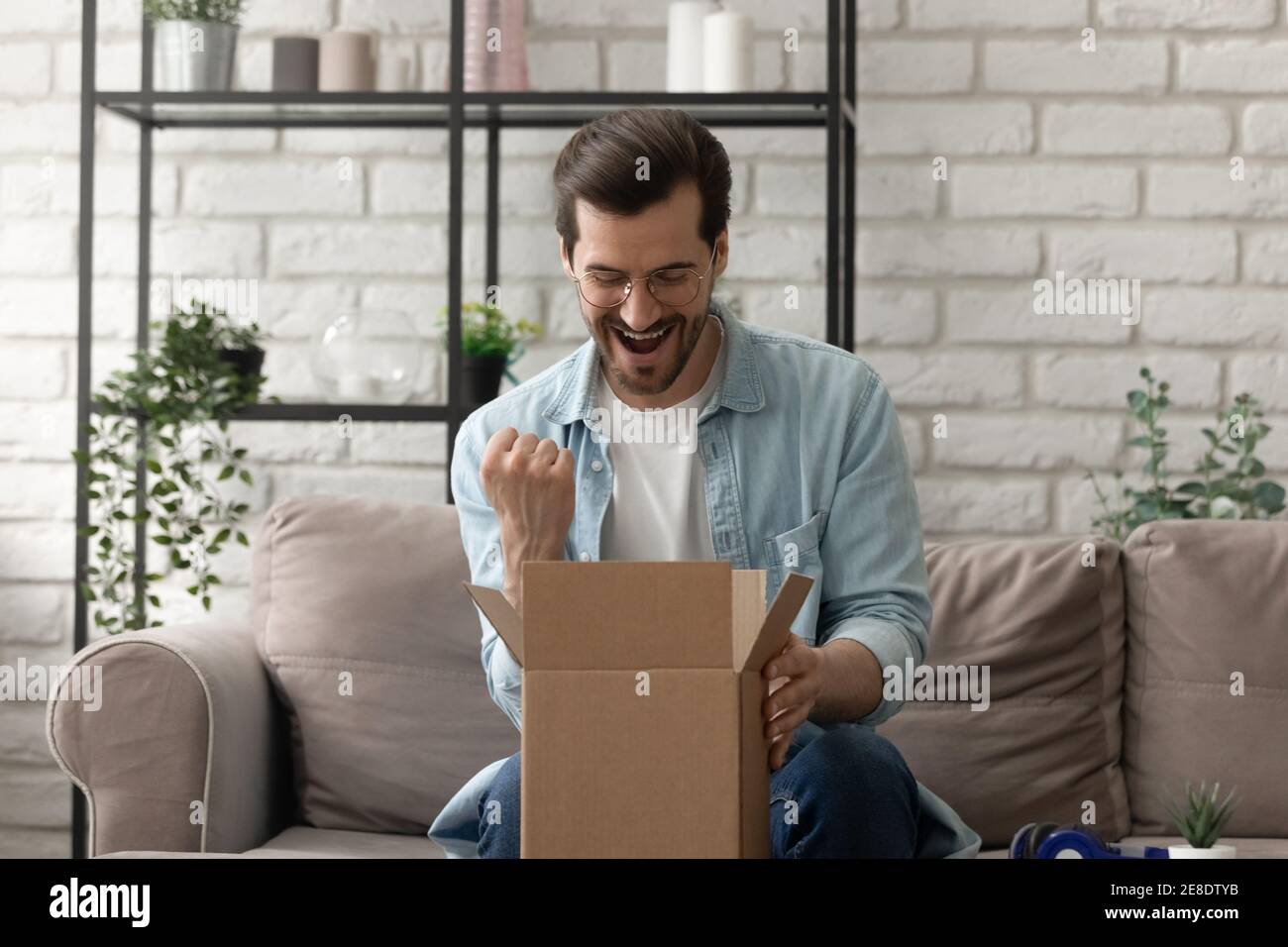 Uomo sopravorato che indossa occhiali guardando in scatola di cartone, pacco ricevuto Foto Stock