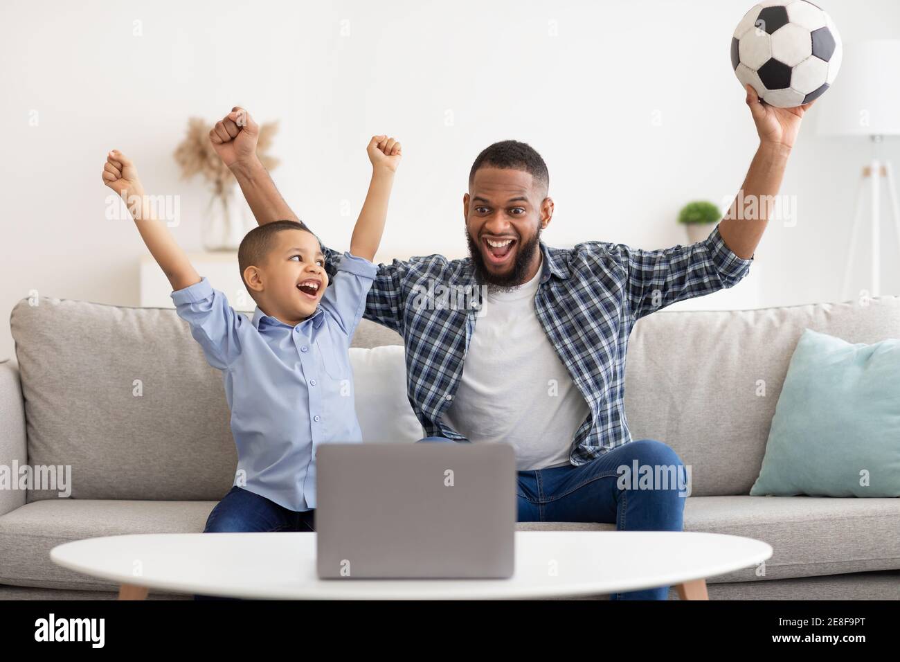 Black Daddy e Son guardano lo sport sul laptop a casa Foto Stock