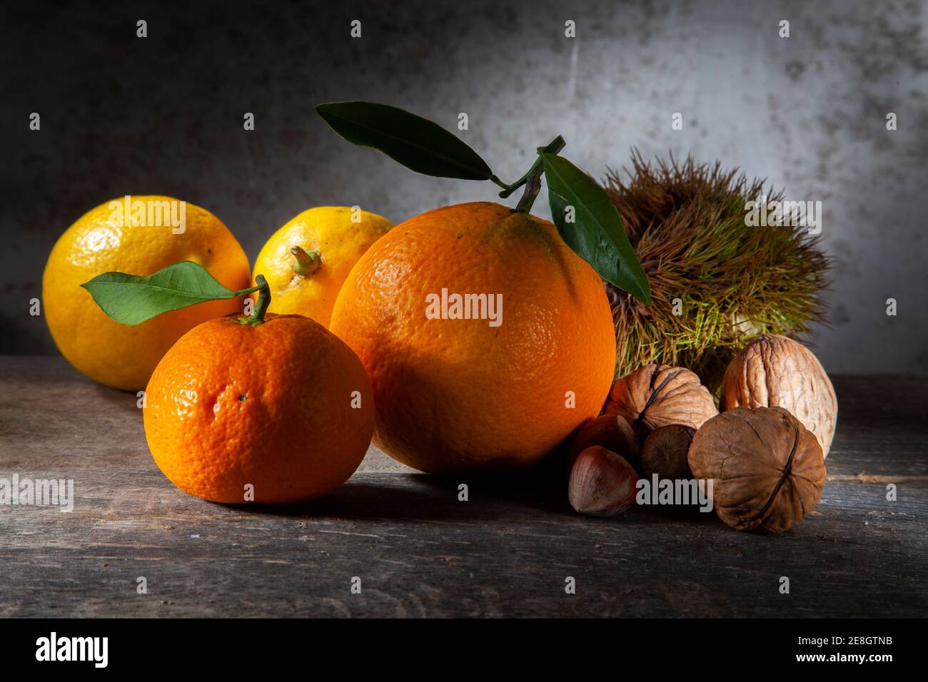 Autunno ancora vita di citrus e noci. Macro Foto di Tangerina arancione e due limoni con tre noci, nocciola e castagno. Su tavola di legno con Foto Stock