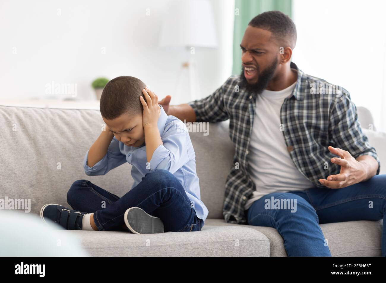 Arrabbiato Padre africano gridando a Son spaventato seduto a casa Foto Stock