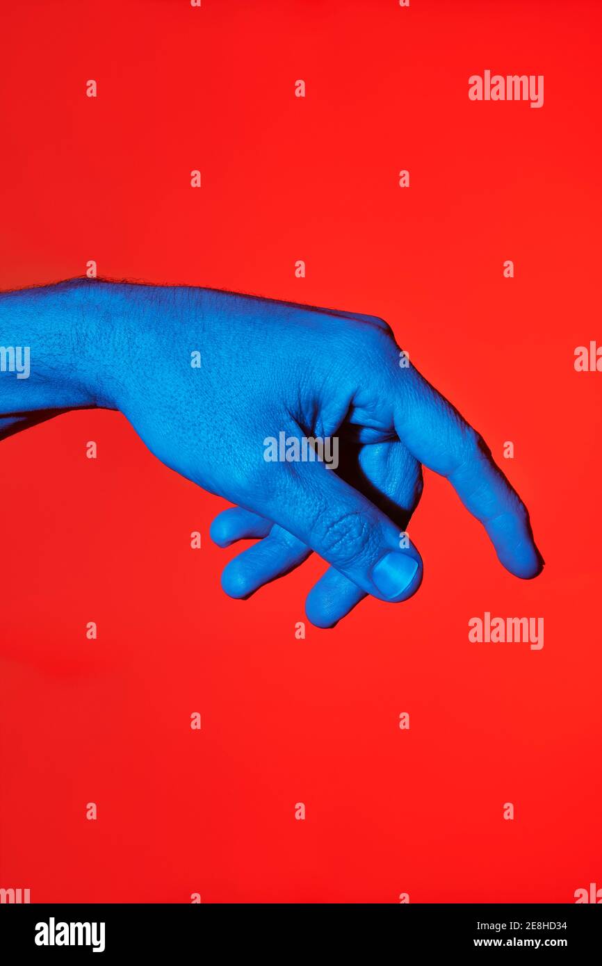 il dito blu dell'uomo che punta verso il basso su sfondo rosso. Foto verticale isolata Foto Stock