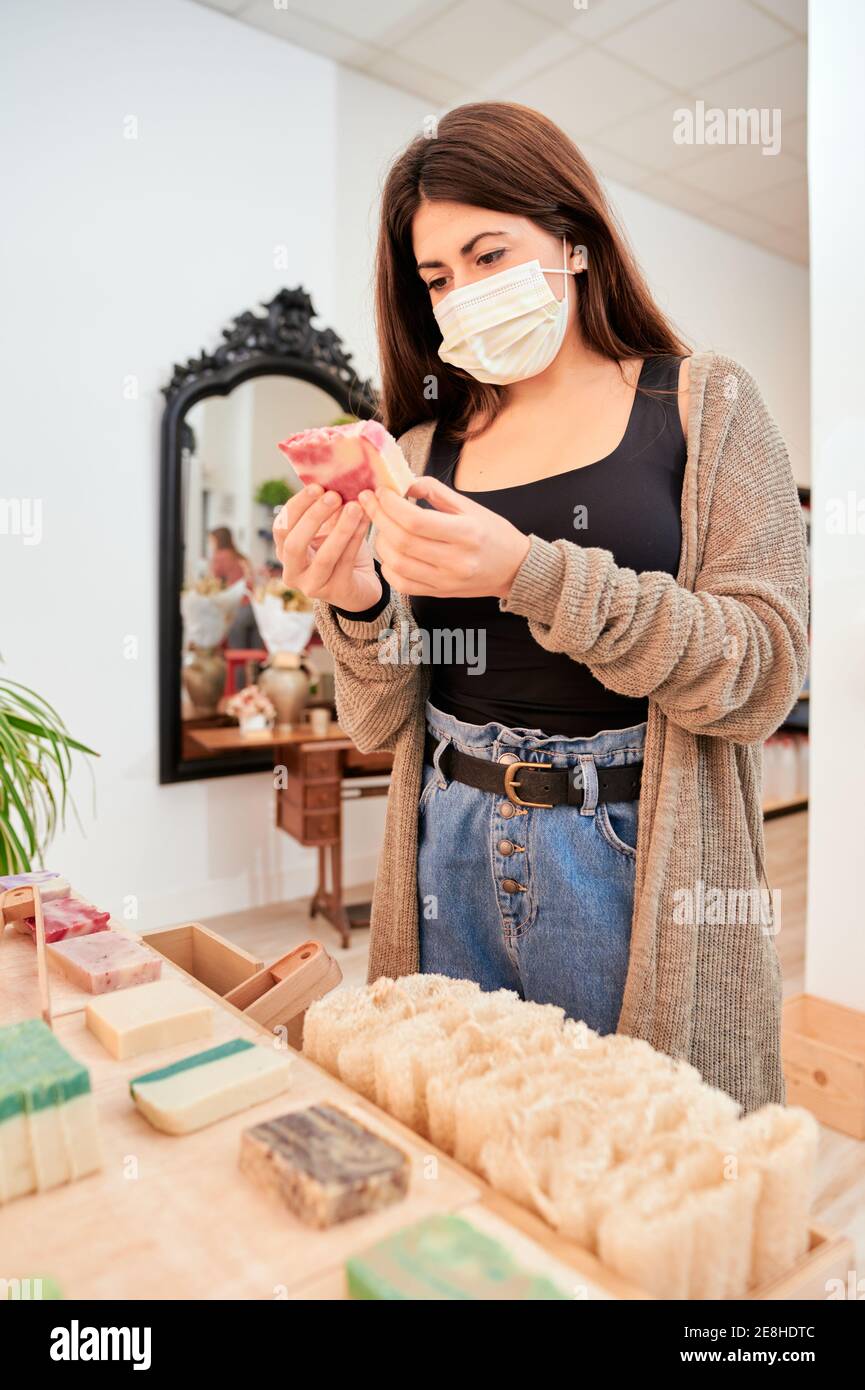Vista laterale di acquirente femminile in maschera medica shopping in conservare con vari sapone biologico fatto in casa Foto Stock