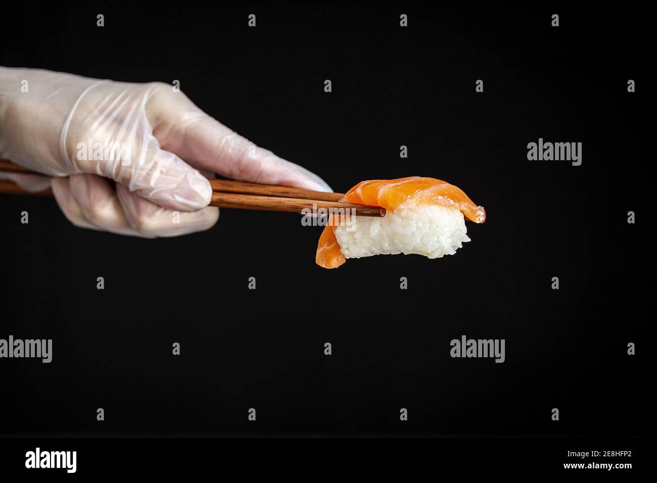 Crop anonimo chef in guanto di lattice che tiene sushi salmone con choppsticks su sfondo nero in un moderno ristorante giapponese Foto Stock