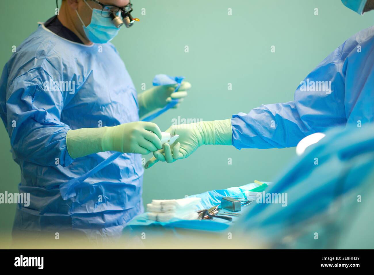 Vista laterale dei medici anonimi di raccolto in abiti chirurgici e. le maschere si aiutano a vicenda mentre si eseguono le operazioni in moderno ospedale Foto Stock