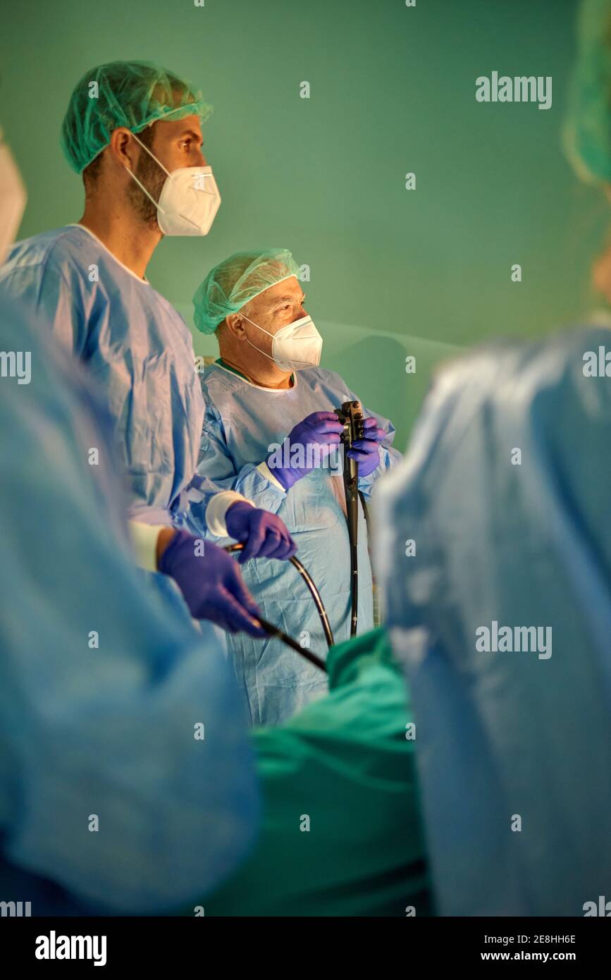 Gruppo di medici anonimi in camici chirurgici e maschere cercando sul monitor durante l'esame del paziente con endoscopio prima dell'uso in clinica moderna Foto Stock