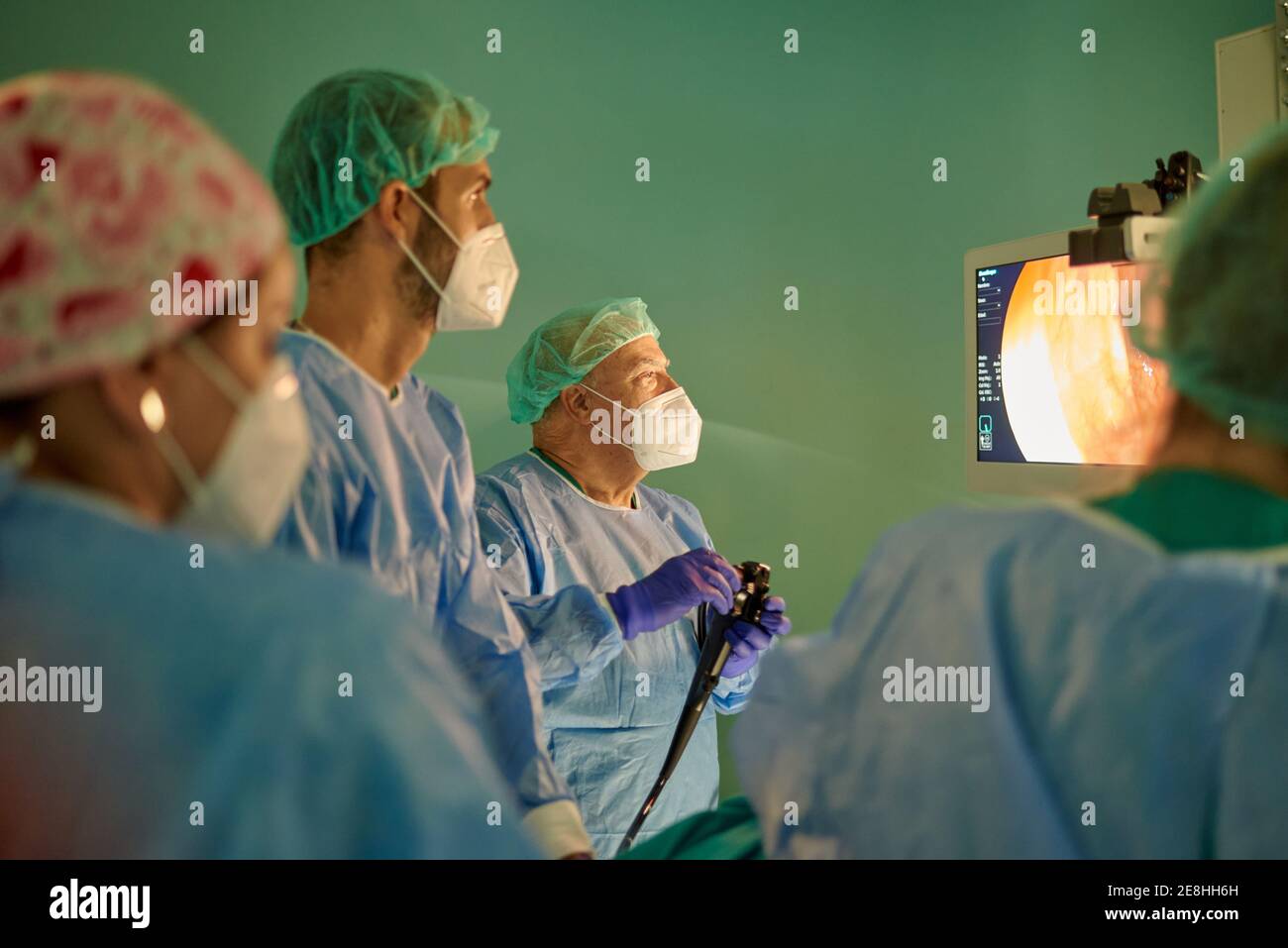 Gruppo di medici anonimi in camici chirurgici e maschere cercando sul monitor durante l'esame del paziente con endoscopio prima dell'uso in clinica moderna Foto Stock