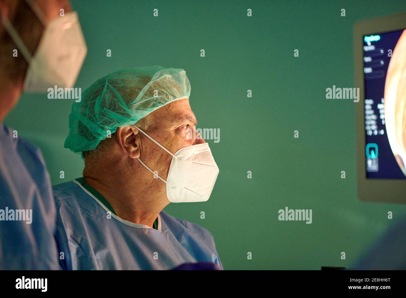 Vista laterale di medici anonimi in camici chirurgici e maschere esaminare il monitor mentre si esamina il paziente con l'endoscopio prima dell'uso in clinica moderna Foto Stock
