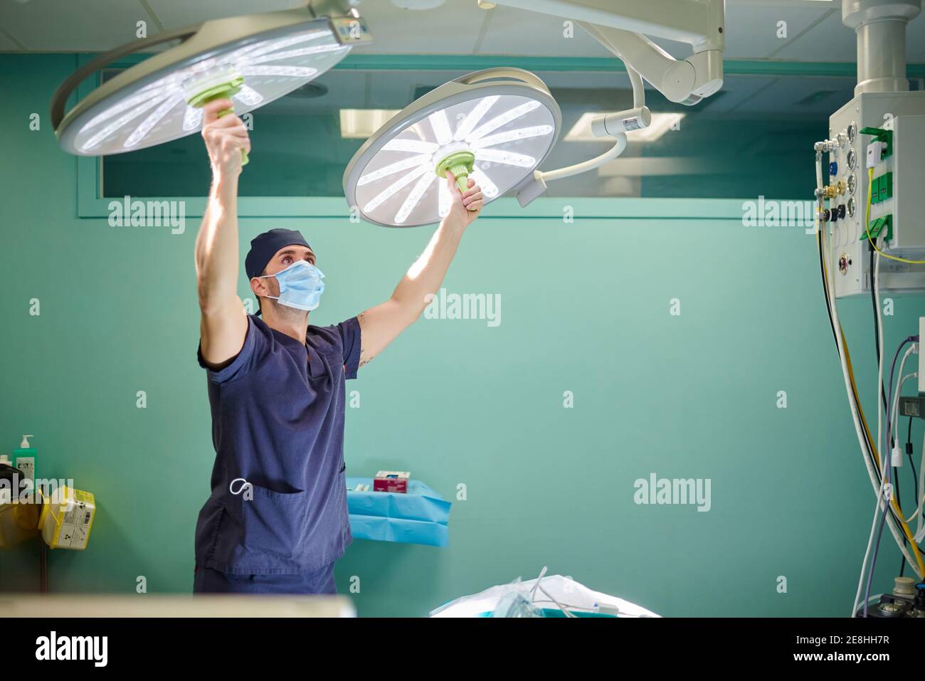 Medica giovane concentrata in uniforme e maschera di regolazione chirurgica luce prima di eseguire il funzionamento in un ospedale moderno Foto Stock