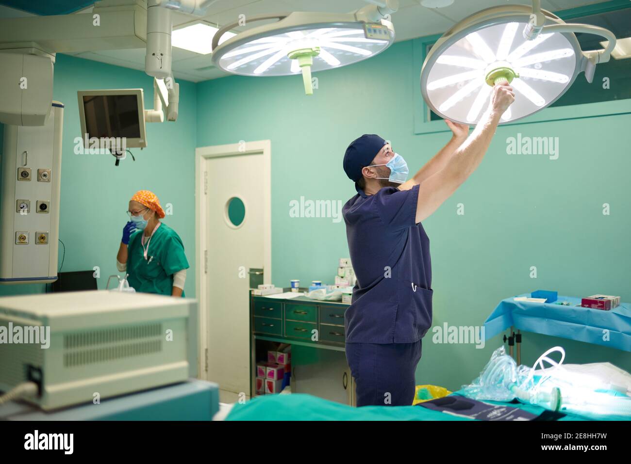 Medica giovane concentrata in uniforme e maschera di regolazione chirurgica luce prima di eseguire il funzionamento in un ospedale moderno Foto Stock