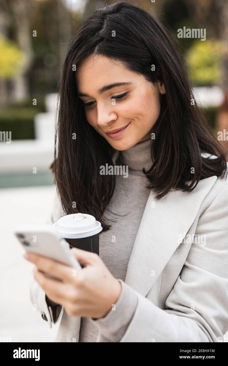 Sorridi l'imprenditore femminile utilizzando lo smartphone in strada mentre beve il caffè Foto Stock