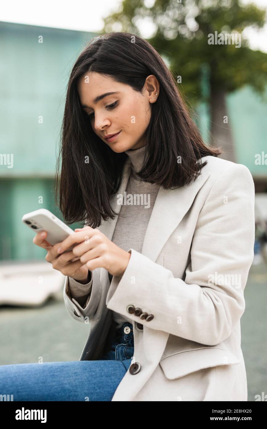 Vista laterale dell'imprenditore femminile concentrato utilizzando uno smartphone in strada durante il controllo dei messaggi e-mail Foto Stock