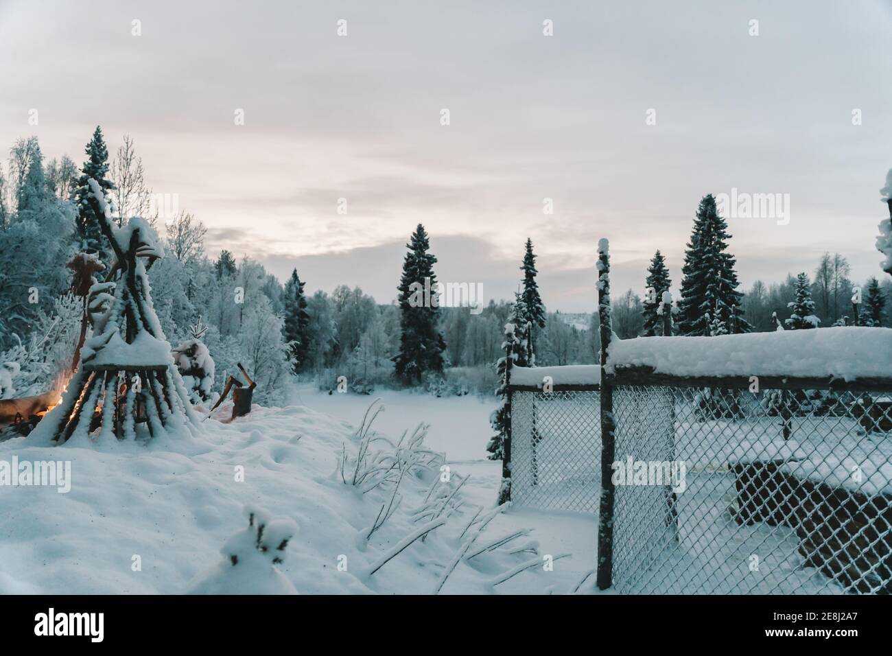 Vista panoramica di lussureggianti alberi di conifere innevate contro i tipi con pali di legno vicino falò in inverno Foto Stock