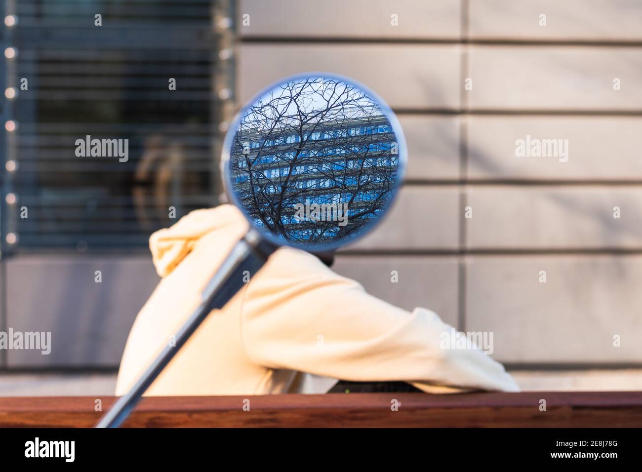 Specchio con il riflesso di edificio residenziale nascondendo faccia di raccolto persona anonima seduta sulla panchina nel parco Foto Stock