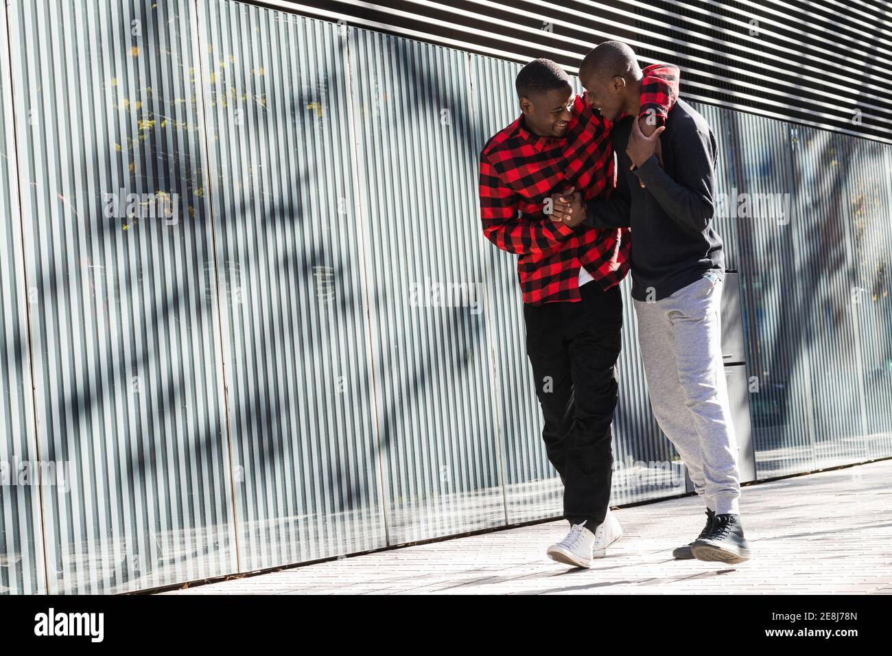 Corpo pieno di gioiosi compagni maschi afroamericani che tengono le mani mentre camminando vicino sulla strada della città Foto Stock